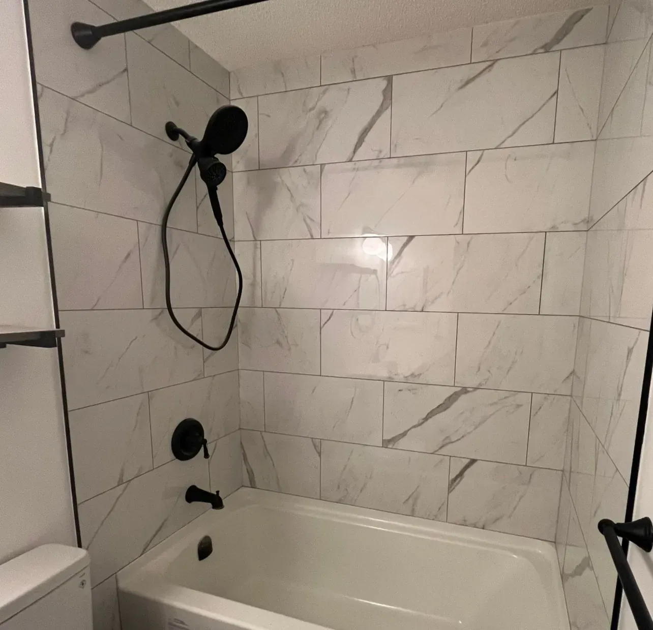 New bathtub with matte black shower head ad marble effect tile in bathroom renovation